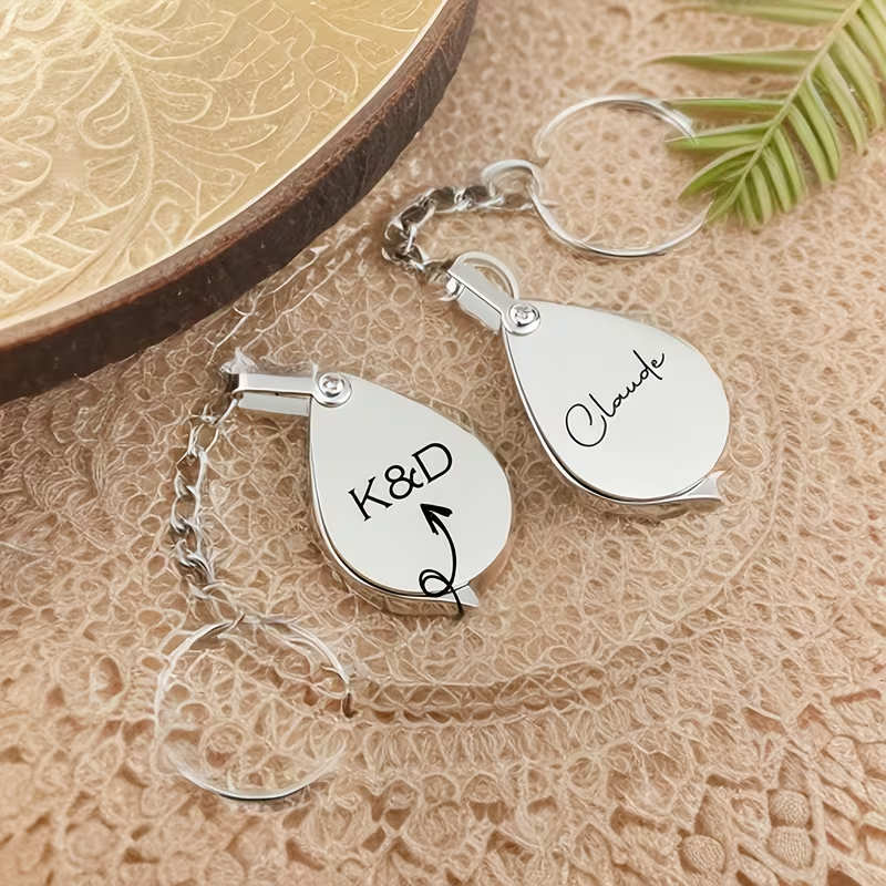 Personalized folding silver magnifying glass keychain with engraved teardrop covers.