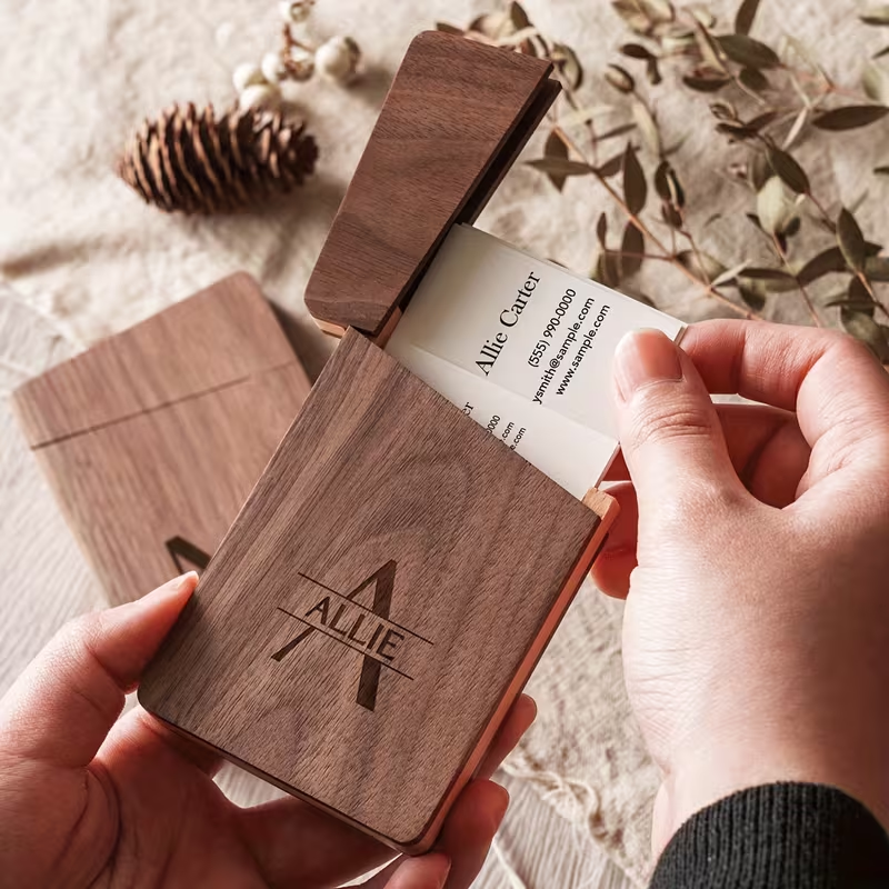 Personalized wood-grain card holder with custom laser engraving, hands pulling a business card